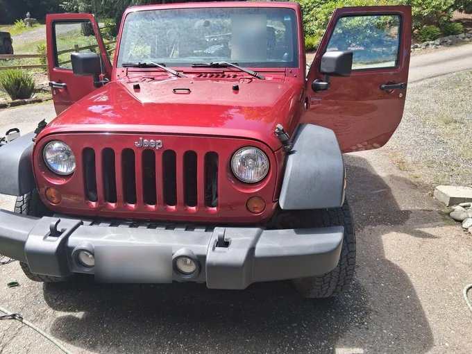 Red Jeep Wrangler in a gravel driveway with its doors open for a detail