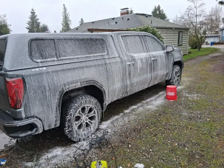 Pickup covered in foam during a hand wash in a gravel driveway