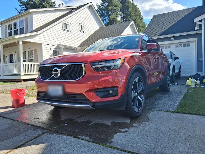 Red Volvo XC40 partway through an exterior detail on a wet driveway, wash bucket and products beside it